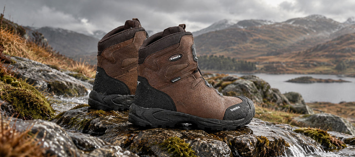 Treksta 8" boots, A pair of brown and black outdoor hiking boots placed on wet rocks with a mountain lake landscape in the background.